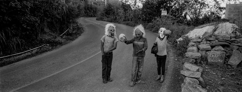 Tres niños con mascaras caminan sobre la carretera