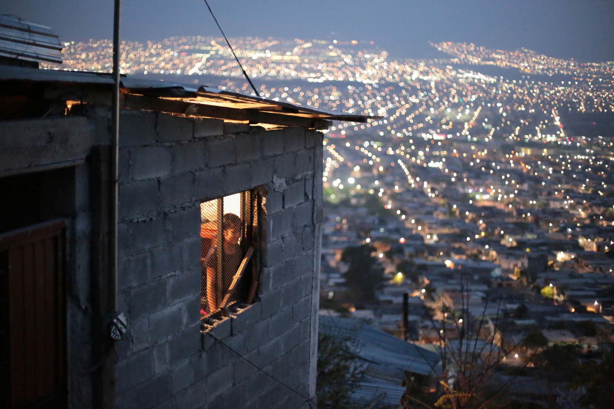 Una niña se asoma desde una casa y de fondo se observa la ciudad